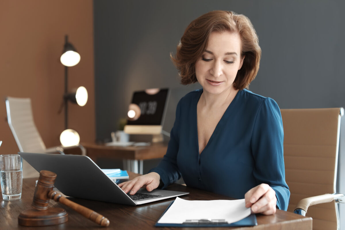 Smiling mature lawyer reading documents while using a laptop in an office