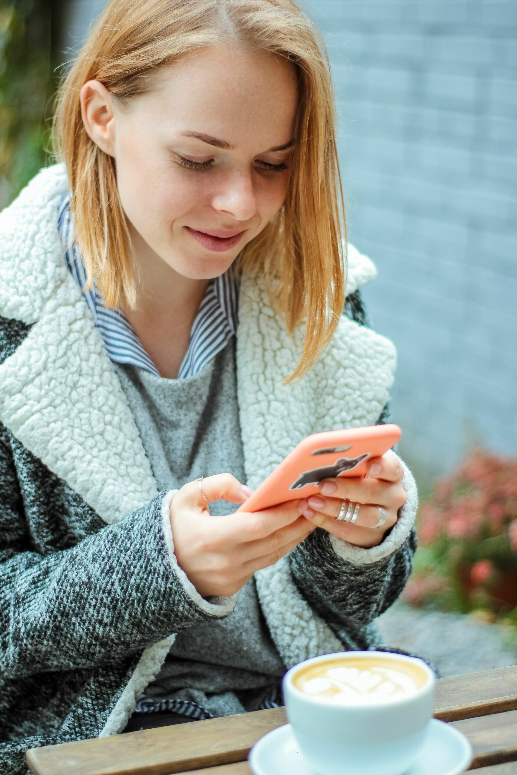 A young woman using a mobile phone to take picture of a cup of coffee